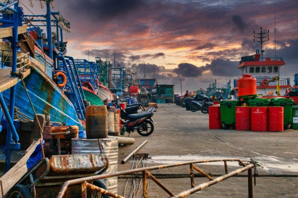 Colorful scene of Jakarta port with ships and containers under a stunning sunset sky.